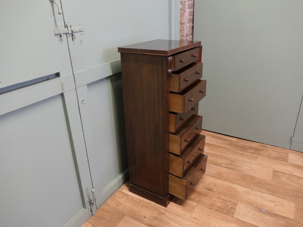 A tall Victorian mahogany Wellington chest featuring seven graduated drawers, turned wooden knob handles, and a side locking bar with a key. View V