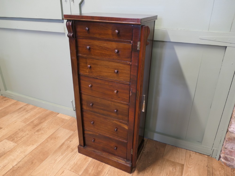 A tall Victorian mahogany Wellington chest featuring seven graduated drawers, turned wooden knob handles, and a side locking bar with a key. View VI