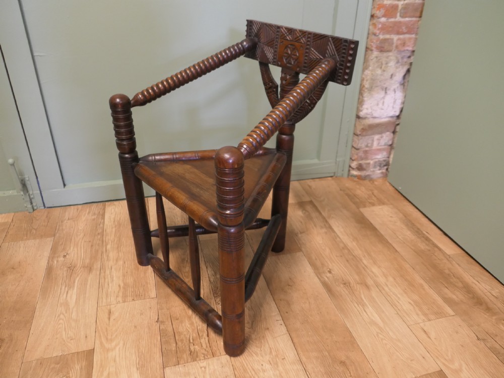 A 19th-century dark oak turners armchair with a triangular seat, heavily turned spindle posts, three legs, and a chip-carved top backrest. View IV