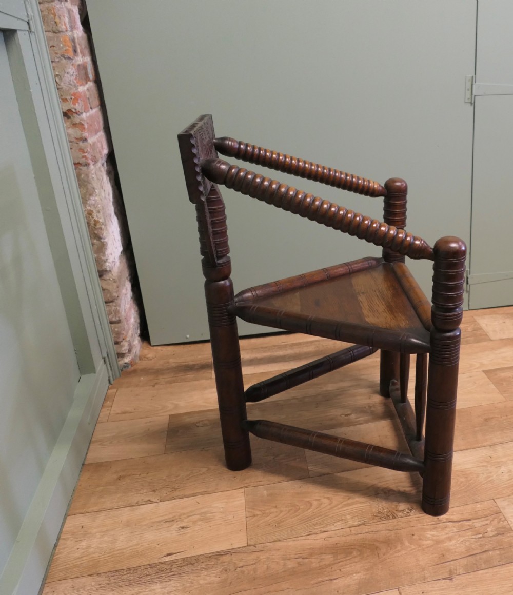 A 19th-century dark oak turners armchair with a triangular seat, heavily turned spindle posts, three legs, and a chip-carved top backrest. View V