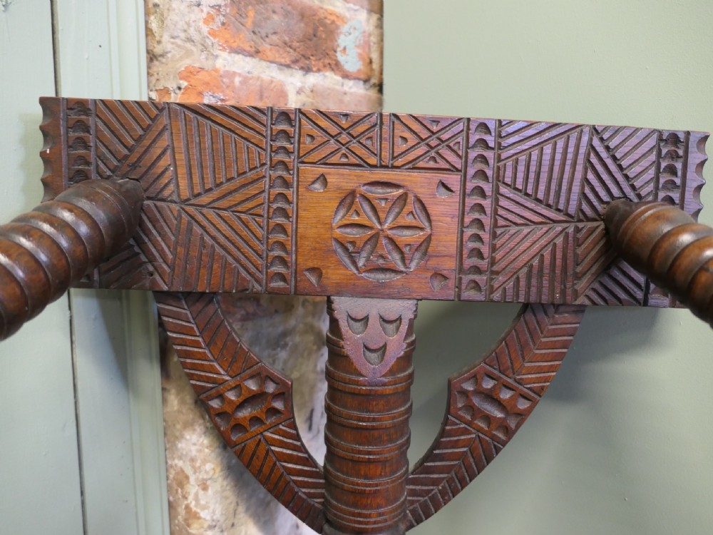 A 19th-century dark oak turners armchair with a triangular seat, heavily turned spindle posts, three legs, and a chip-carved top backrest. View VI