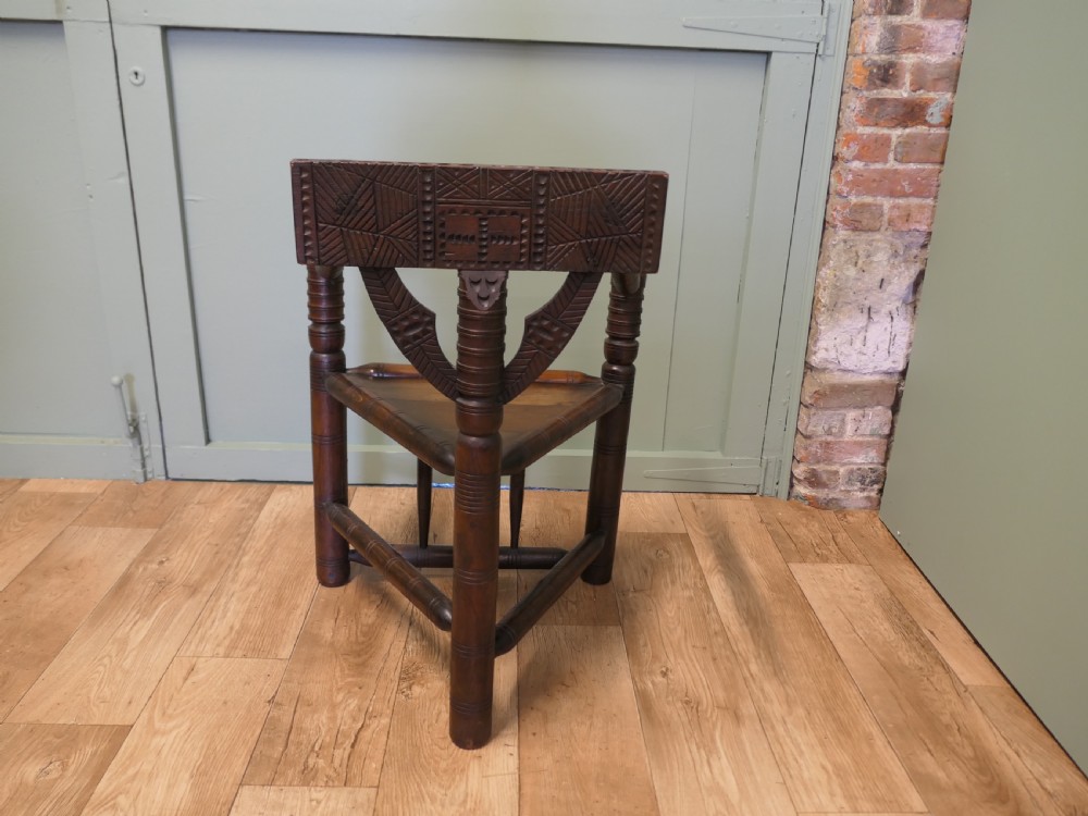 A 19th-century dark oak turners armchair with a triangular seat, heavily turned spindle posts, three legs, and a chip-carved top backrest. View VII