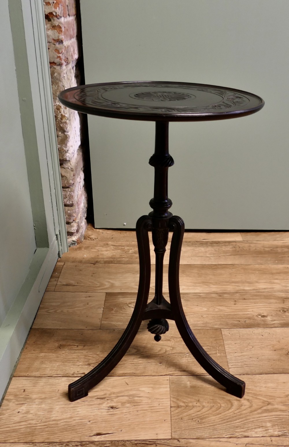 A dark mahogany Art Nouveau wine table featuring a carved circular top, turned stem, and three swept legs with a carved central pendant.