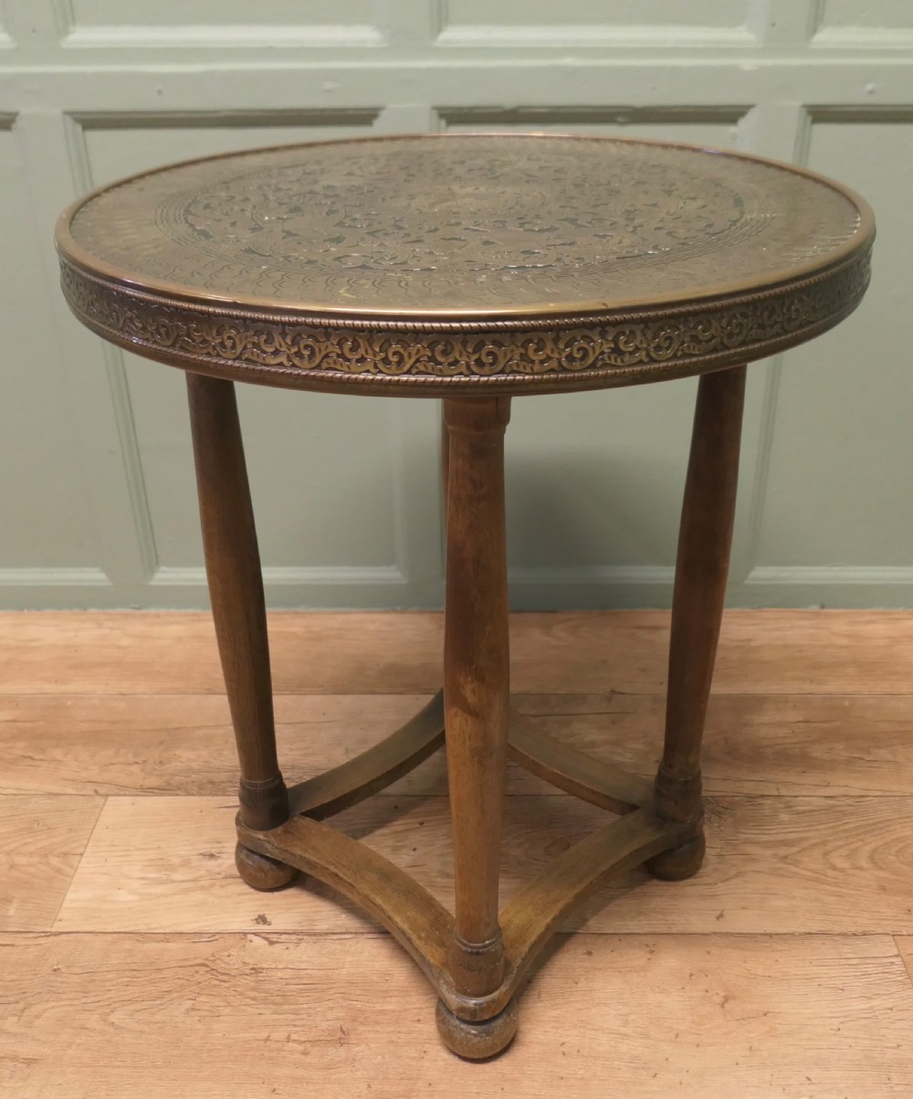 A circular Arts and Crafts side table with an embossed brass top displaying a peacock motif on a turned timber base.