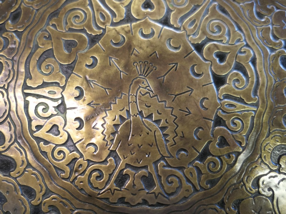 A circular Arts and Crafts side table with an embossed brass top displaying a peacock motif on a turned timber base. View II