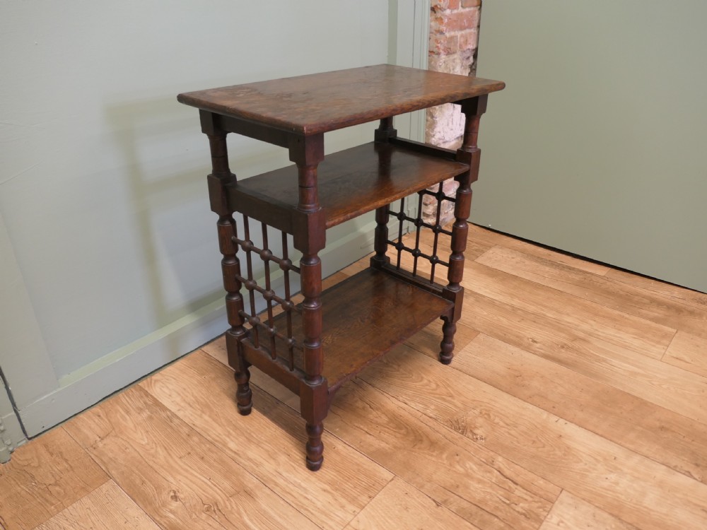 A dark oak three-tier Arts and Crafts side table featuring turned legs and spindled side galleries.