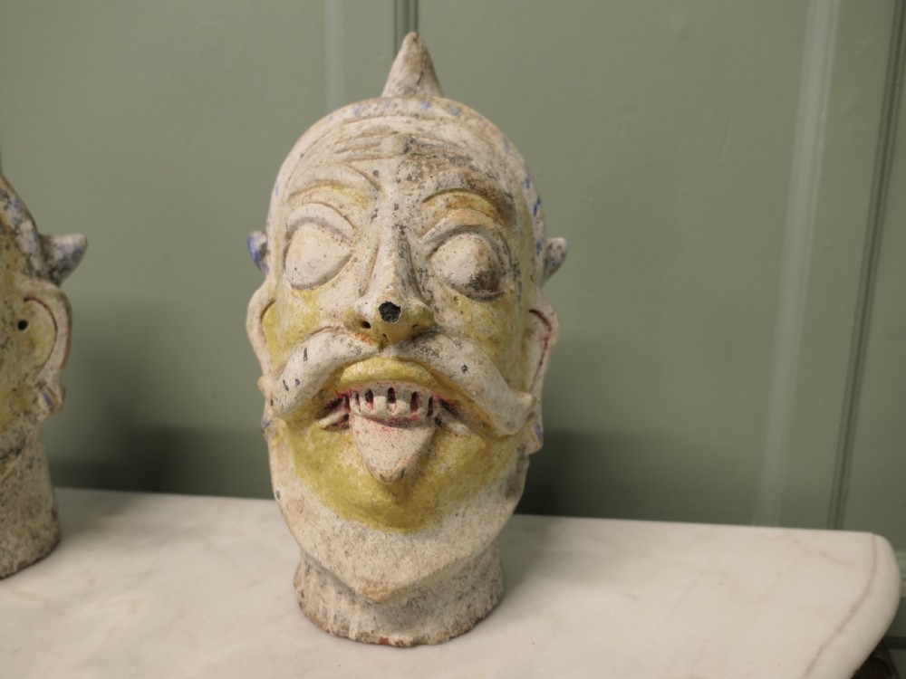 Pair of painted Indian terracotta tent pole tops sculpted as expressive facial heads with moustaches and conical crowns. View VI