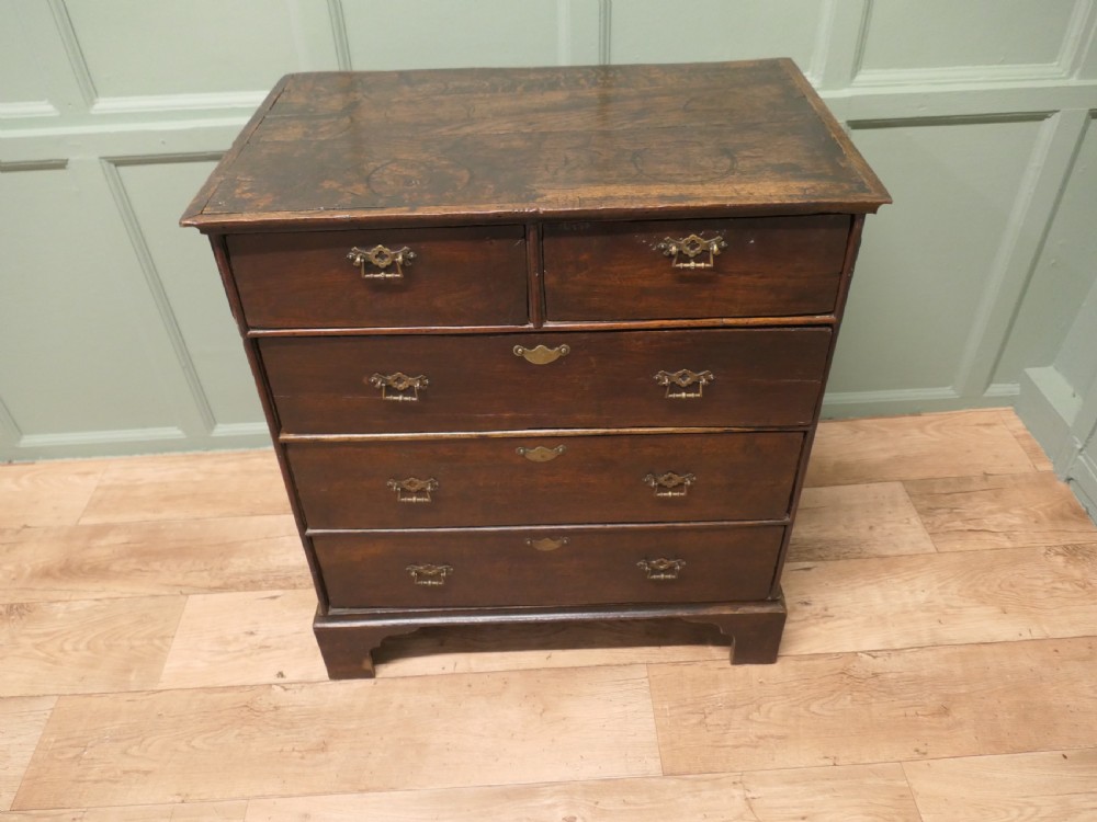 A late 18th-century Georgian dark oak chest of drawers featuring a two-short over three-long drawer configuration, brass drop handles, and bracket feet.