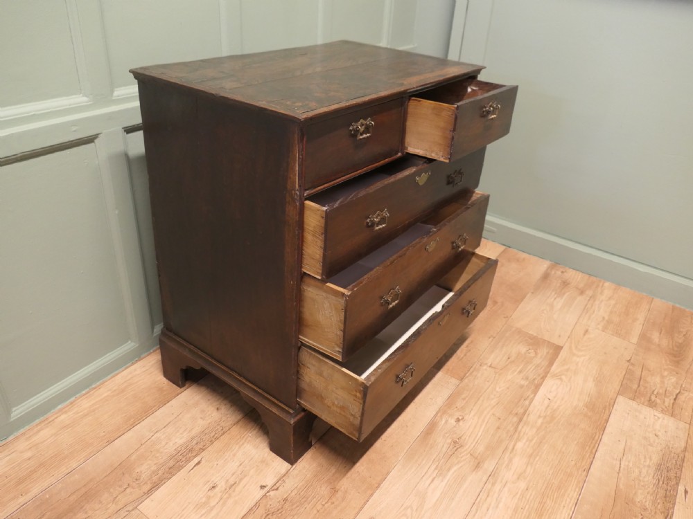 A late 18th-century Georgian dark oak chest of drawers featuring a two-short over three-long drawer configuration, brass drop handles, and bracket feet. View II