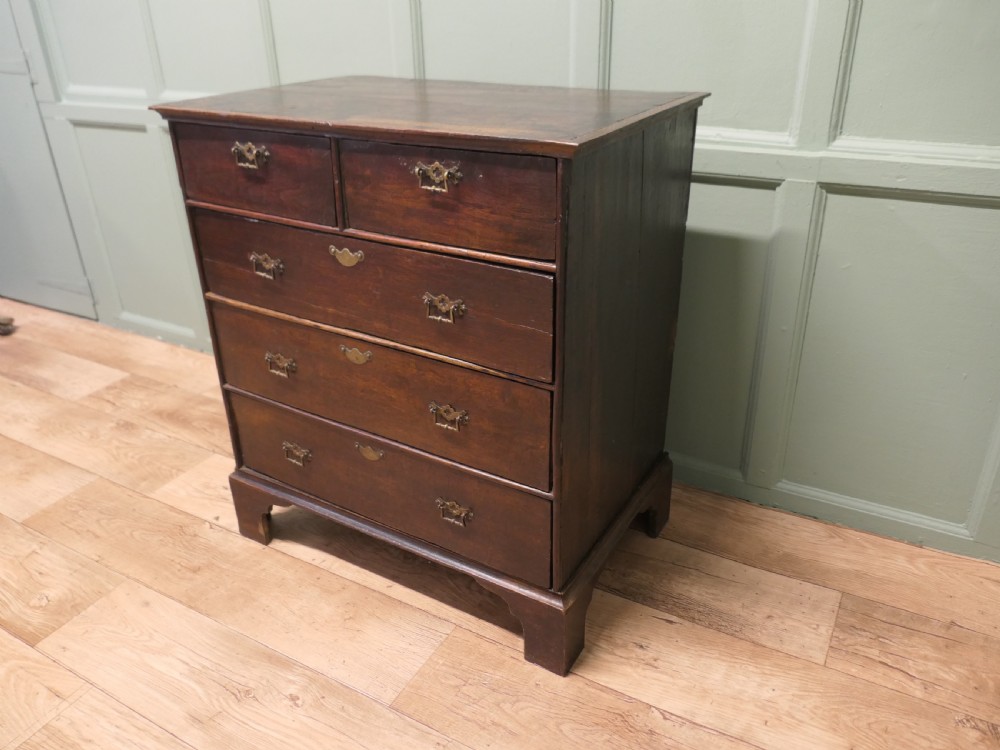 A late 18th-century Georgian dark oak chest of drawers featuring a two-short over three-long drawer configuration, brass drop handles, and bracket feet. View V