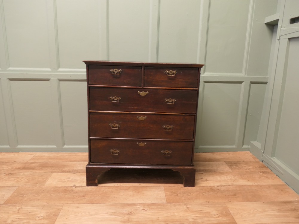 A late 18th-century Georgian dark oak chest of drawers featuring a two-short over three-long drawer configuration, brass drop handles, and bracket feet. View VI