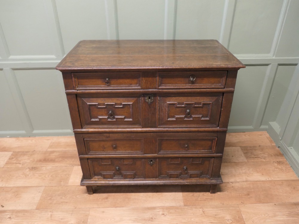 An 18th century dark oak chest of drawers featuring geometric panelled drawer fronts, brass drop handles, and panelled sides. View III