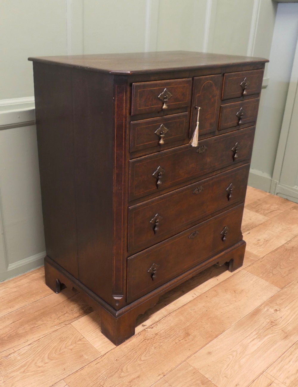An 18th-century Georgian walnut and oak chest of drawers featuring inlaid drawer fronts, brass teardrop handles, a central cupboard section, and bracket feet. View II