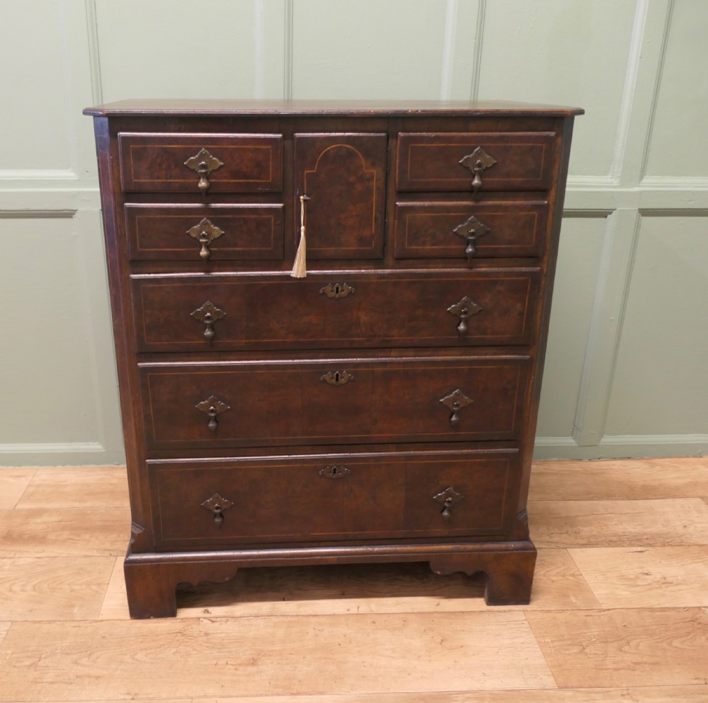 An 18th-century Georgian walnut and oak chest of drawers featuring inlaid drawer fronts, brass teardrop handles, a central cupboard section, and bracket feet. View III