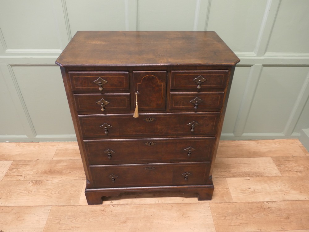 An 18th-century Georgian walnut and oak chest of drawers featuring inlaid drawer fronts, brass teardrop handles, a central cupboard section, and bracket feet. View IV
