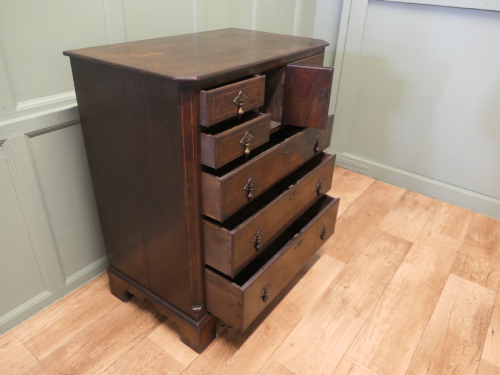 An 18th-century Georgian walnut and oak chest of drawers featuring inlaid drawer fronts, brass teardrop handles, a central cupboard section, and bracket feet. View V