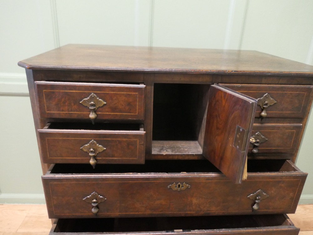 An 18th-century Georgian walnut and oak chest of drawers featuring inlaid drawer fronts, brass teardrop handles, a central cupboard section, and bracket feet. View VI