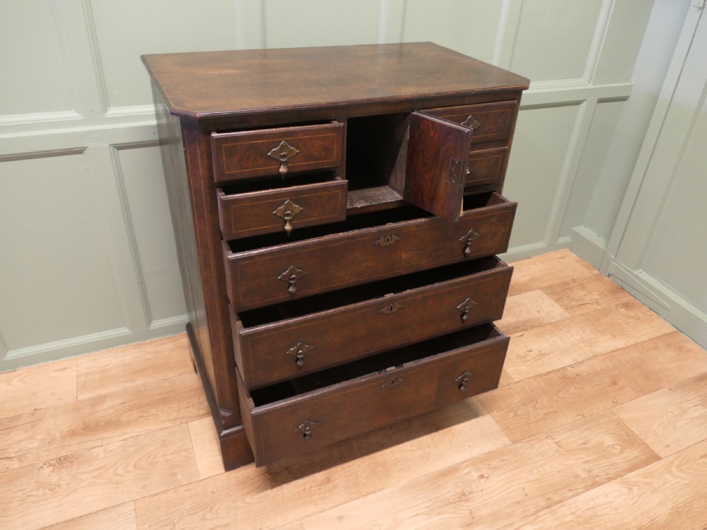 An 18th-century Georgian walnut and oak chest of drawers featuring inlaid drawer fronts, brass teardrop handles, a central cupboard section, and bracket feet. View VII