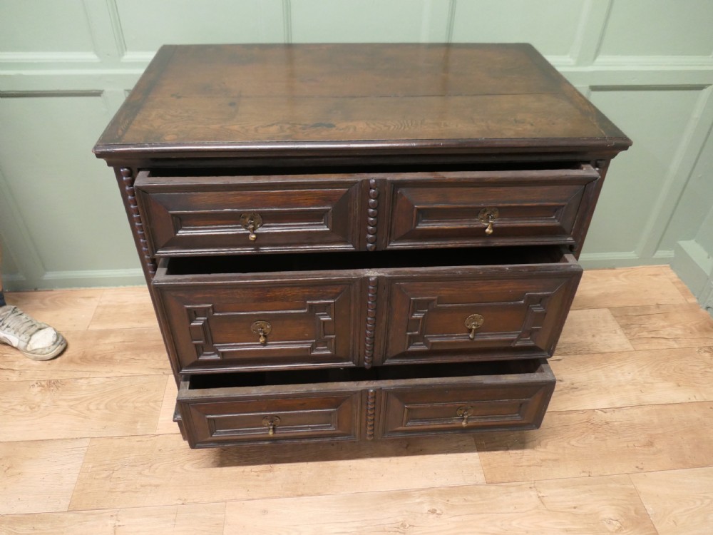 A dark oak chest of drawers featuring geometric moulded panels, brass teardrop handles, and vertical bobbin moulding. View IV