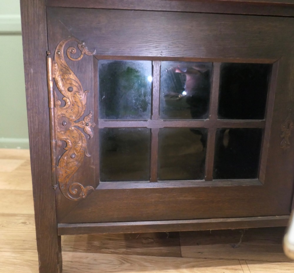 An Arts and Crafts dark oak sideboard featuring a slatted upper gallery, central mirror, two small upper cabinets, frieze drawers, and lower cupboards with strap hinges. View III