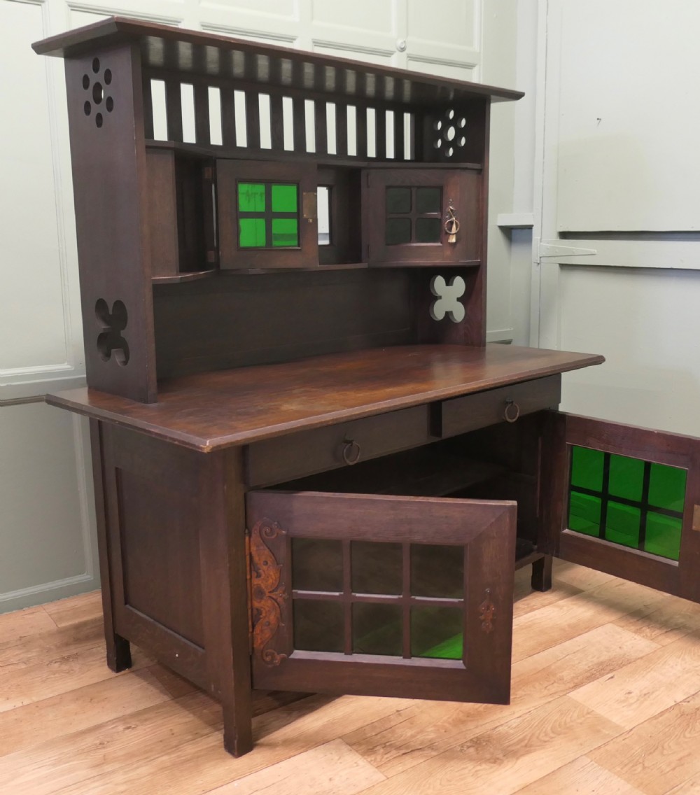 An Arts and Crafts dark oak sideboard featuring a slatted upper gallery, central mirror, two small upper cabinets, frieze drawers, and lower cupboards with strap hinges. View VI