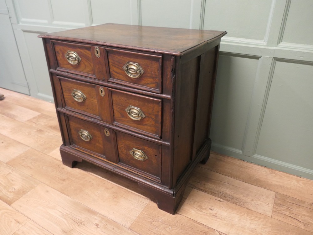 An 18th-century country elm chest of drawers with three moulded drawer fronts, brass drop handles, keyhole escutcheons, and bracket feet. View III