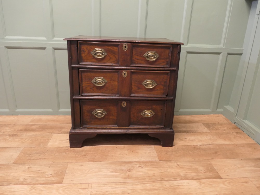 An 18th-century country elm chest of drawers with three moulded drawer fronts, brass drop handles, keyhole escutcheons, and bracket feet. View V
