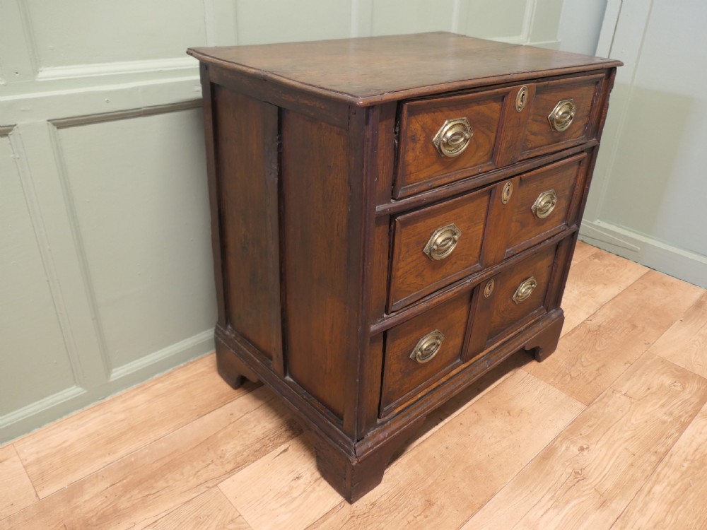 An 18th-century country elm chest of drawers with three moulded drawer fronts, brass drop handles, keyhole escutcheons, and bracket feet. View VI