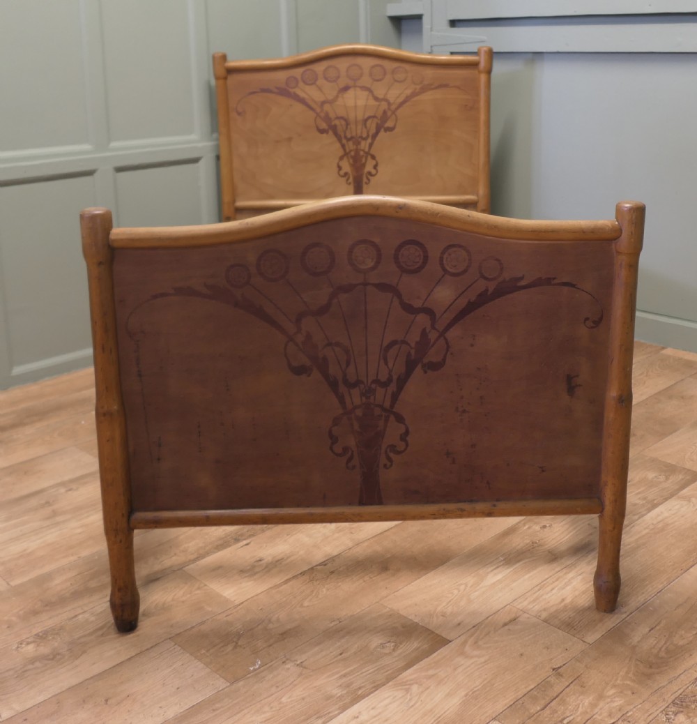 An antique Vienna Secession single wooden bedstead featuring arched headboard and footboard panels decorated with stylised botanical marquetry motifs.