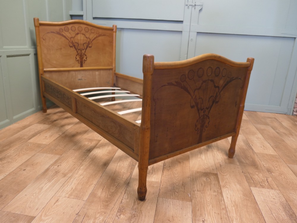 An antique Vienna Secession single wooden bedstead featuring arched headboard and footboard panels decorated with stylised botanical marquetry motifs. View IV