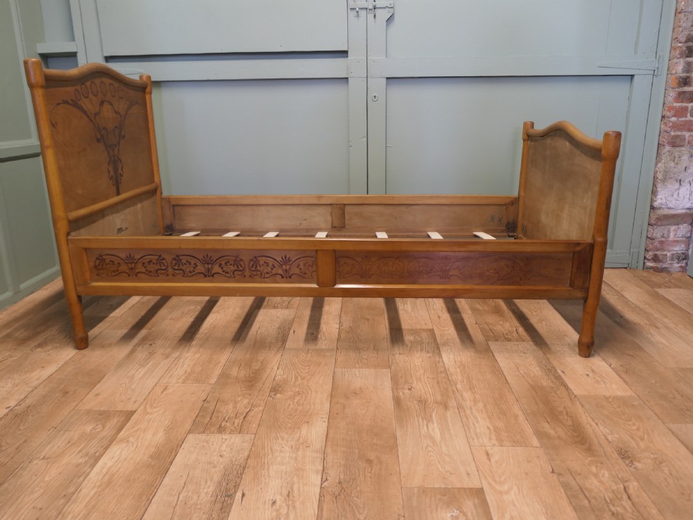An antique Vienna Secession single wooden bedstead featuring arched headboard and footboard panels decorated with stylised botanical marquetry motifs. View V