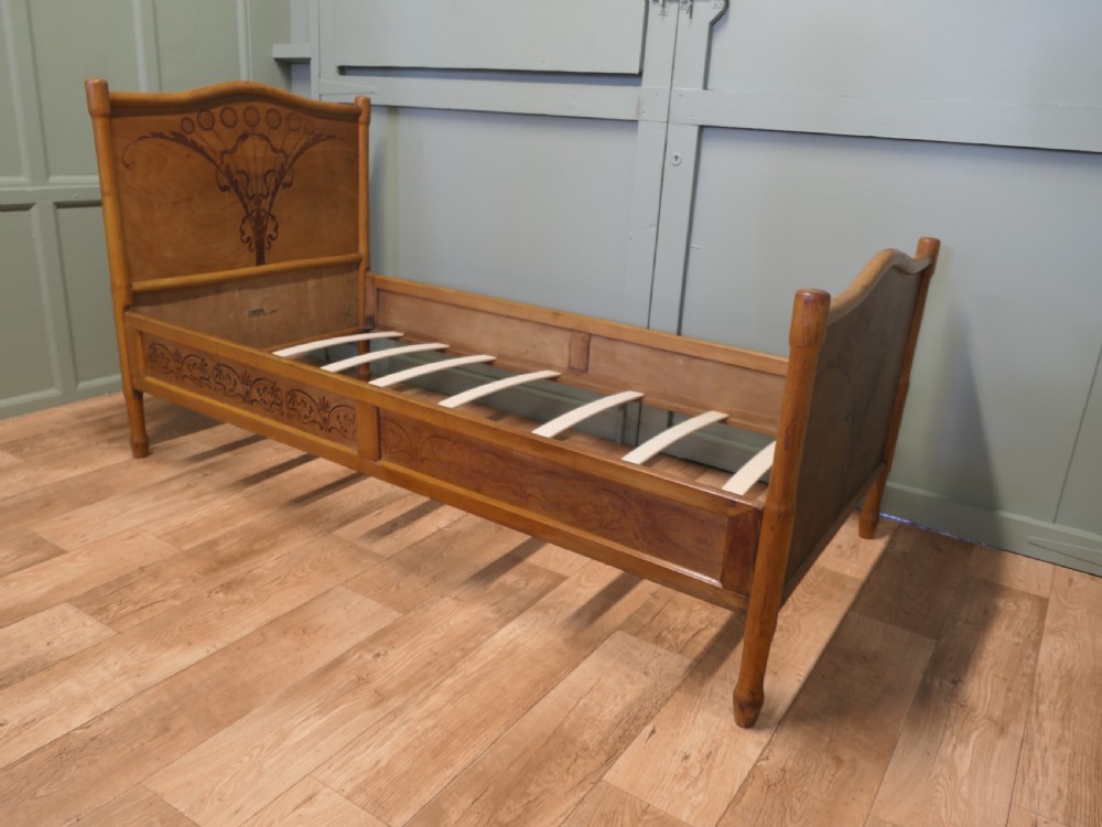 An antique Vienna Secession single wooden bedstead featuring arched headboard and footboard panels decorated with stylised botanical marquetry motifs. View VI