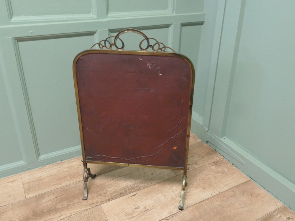 An Art Deco brass fire screen featuring a bevelled glass mirror panel with a cut sunburst motif set on cast metal feet. View III