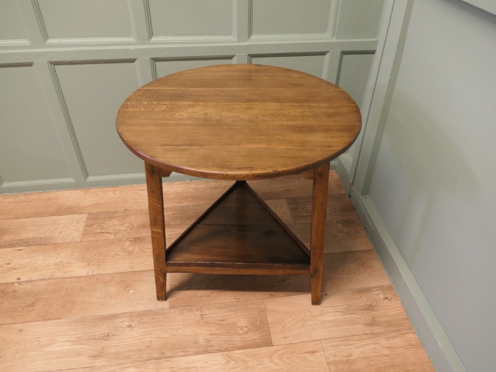 A Georgian oak cricket table featuring a circular top, three straight square legs, and a lower triangular under-shelf.