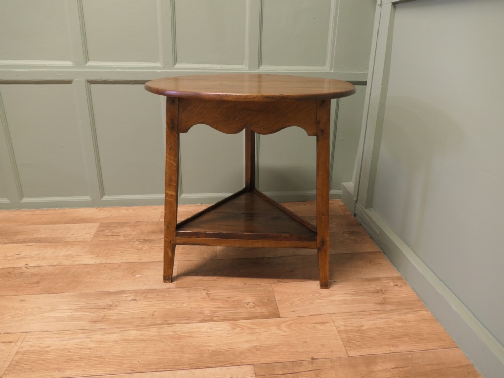A Georgian oak cricket table featuring a circular top, three straight square legs, and a lower triangular under-shelf. View II