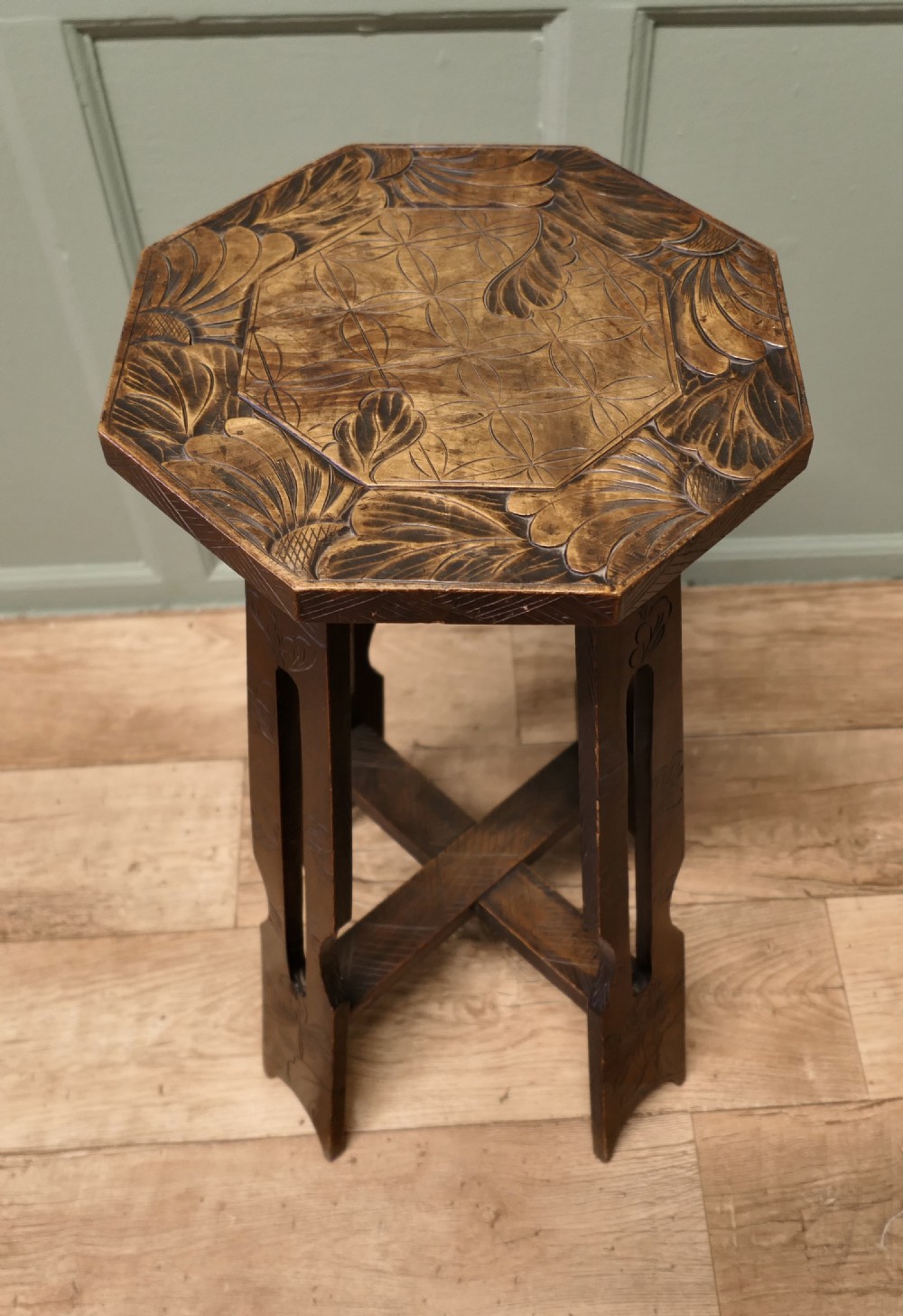 An Arts and Crafts dark elm plant stand featuring an octagonal carved top, stylised floral carving on four pierced legs, and an X-frame stretcher. View II