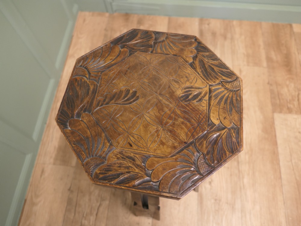 An Arts and Crafts dark elm plant stand featuring an octagonal carved top, stylised floral carving on four pierced legs, and an X-frame stretcher. View V