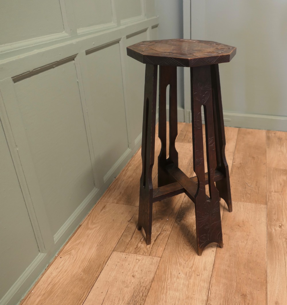 An Arts and Crafts dark elm plant stand featuring an octagonal carved top, stylised floral carving on four pierced legs, and an X-frame stretcher. View VI