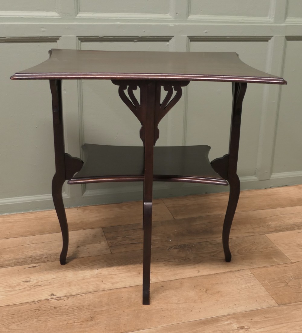 An Arts and Crafts mahogany occasional table featuring a flared rectangular top, pierced corner brackets, a lower tier shelf, and curved legs.