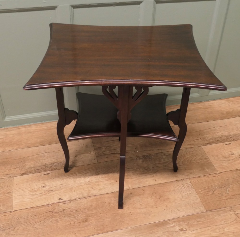An Arts and Crafts mahogany occasional table featuring a flared rectangular top, pierced corner brackets, a lower tier shelf, and curved legs. View II