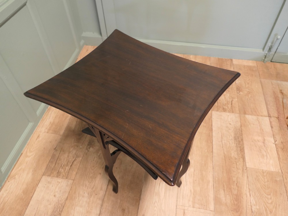 An Arts and Crafts mahogany occasional table featuring a flared rectangular top, pierced corner brackets, a lower tier shelf, and curved legs. View III