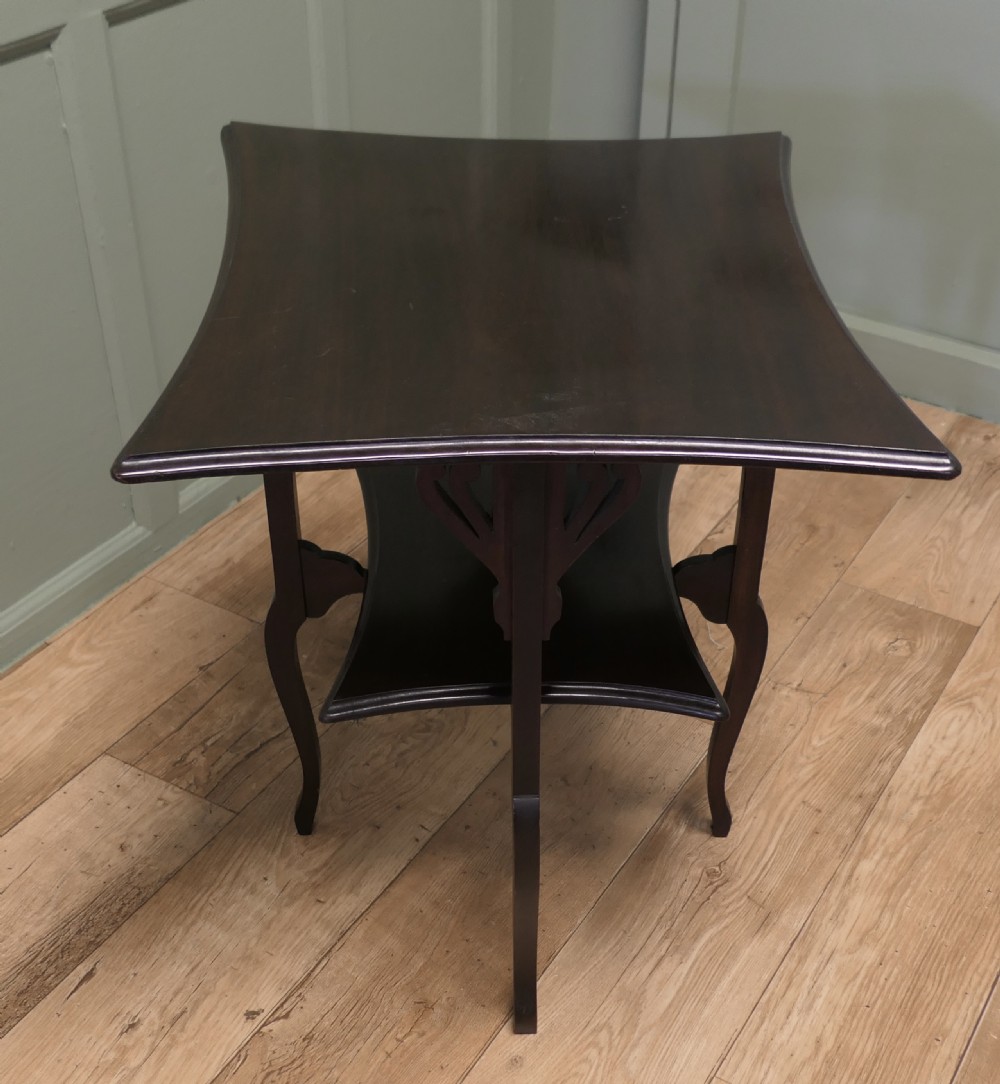 An Arts and Crafts mahogany occasional table featuring a flared rectangular top, pierced corner brackets, a lower tier shelf, and curved legs. View IV