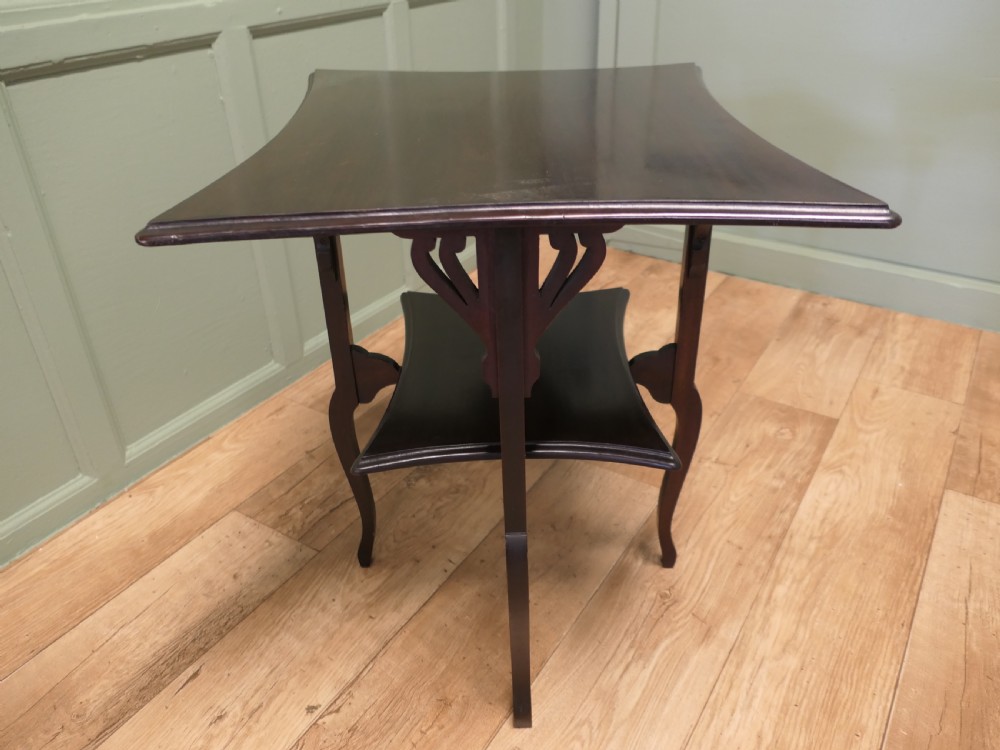 An Arts and Crafts mahogany occasional table featuring a flared rectangular top, pierced corner brackets, a lower tier shelf, and curved legs. View V