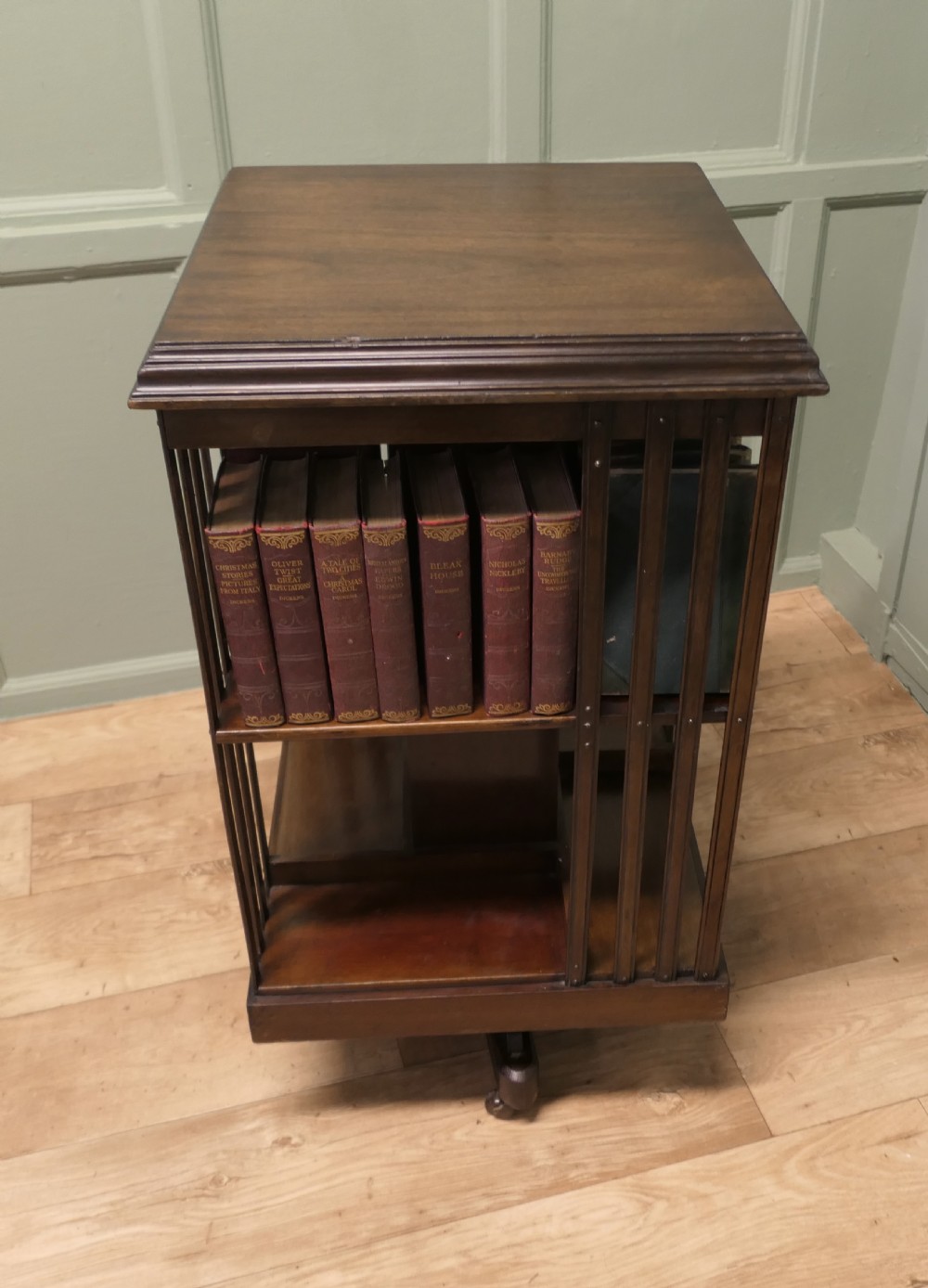 A square mahogany revolving library bookcase featuring vertical slatted sides, three tiered shelves, and castors on the base. View IV