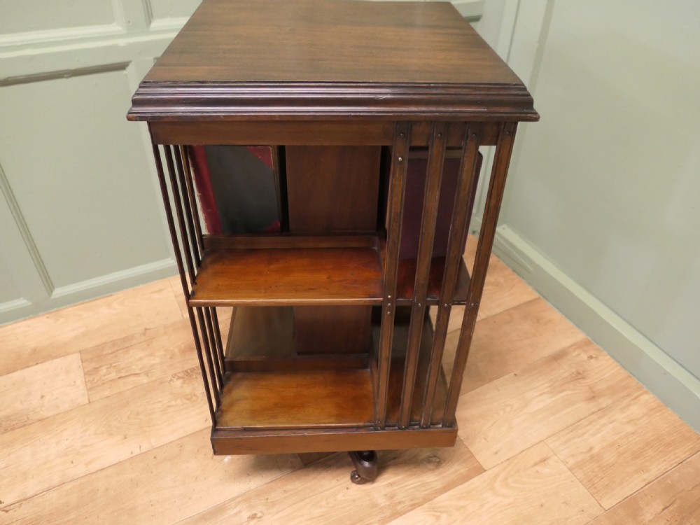 A square mahogany revolving library bookcase featuring vertical slatted sides, three tiered shelves, and castors on the base. View V