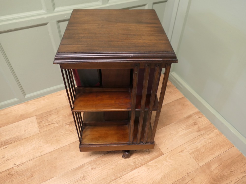 A square mahogany revolving library bookcase featuring vertical slatted sides, three tiered shelves, and castors on the base. View VII