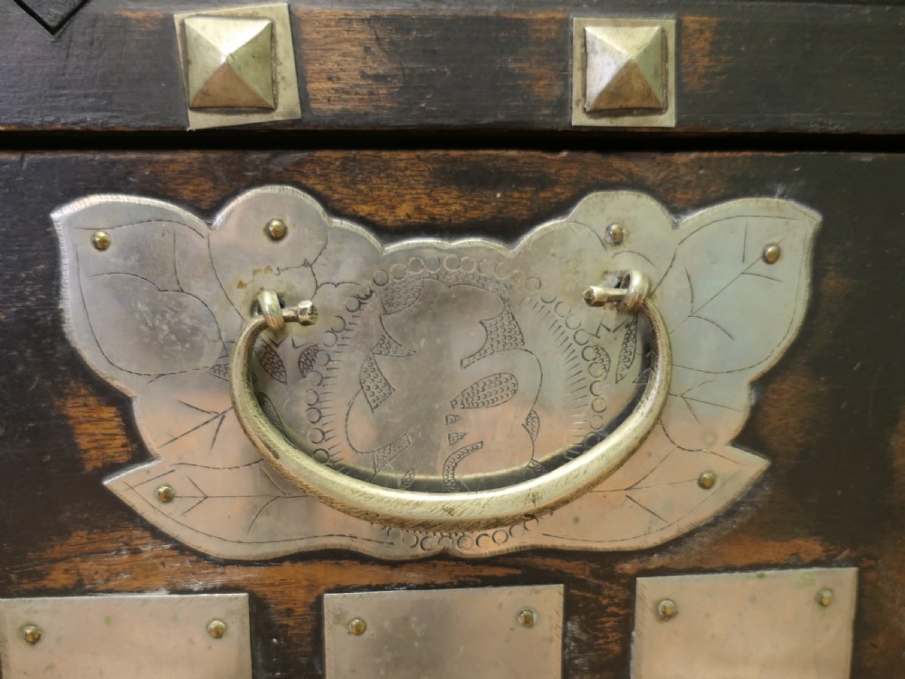 A dark brown wooden Korean Bandaji chest adorned with elaborate silver-coloured brass plating, geometric studs, etched metal panels, and three top drawers. View IV