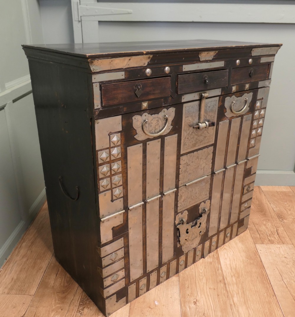 A dark brown wooden Korean Bandaji chest adorned with elaborate silver-coloured brass plating, geometric studs, etched metal panels, and three top drawers. View VI