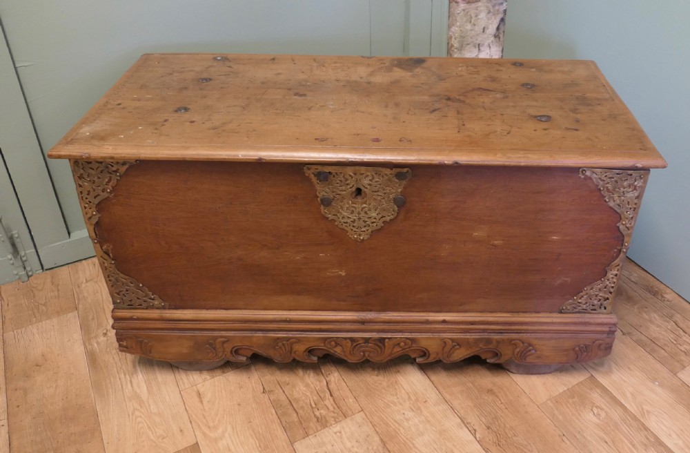 A rectangular carved elm wood storage coffer featuring decorative pierced brass corner mounts and a central lockplate above an ornate carved apron. View III