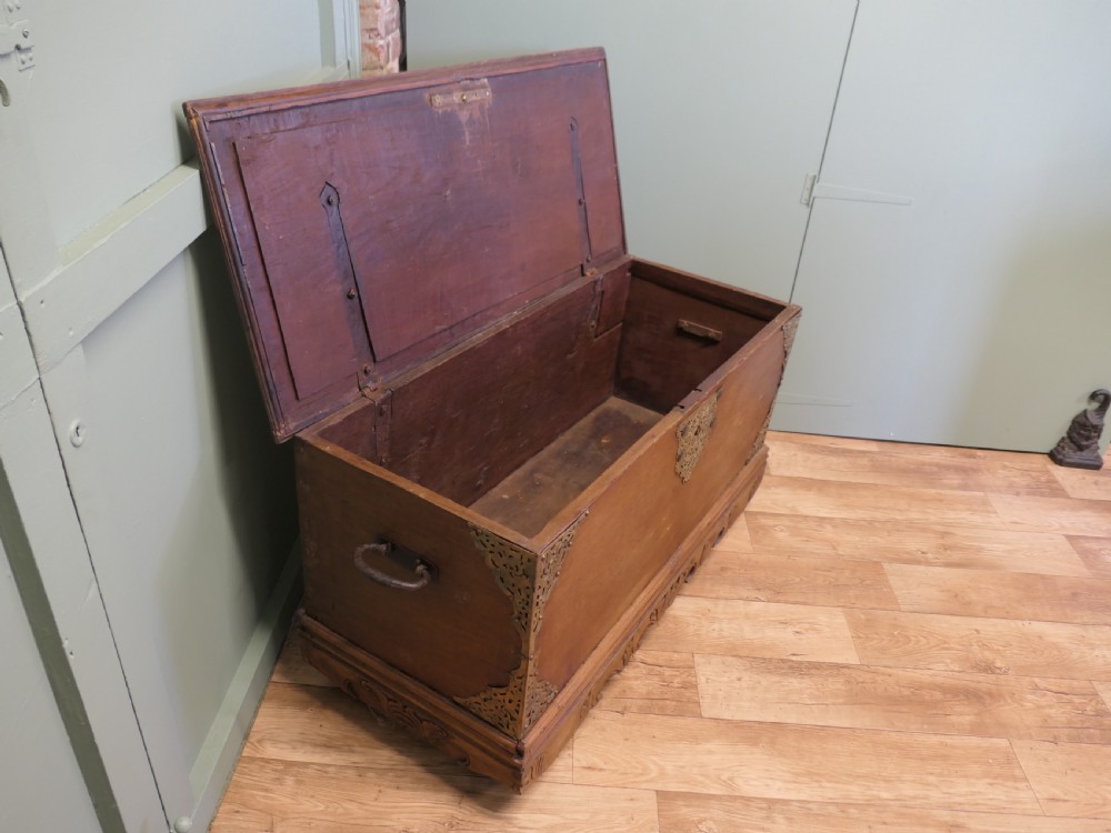 A rectangular carved elm wood storage coffer featuring decorative pierced brass corner mounts and a central lockplate above an ornate carved apron. View IV
